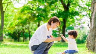 公園で子どもと向き合うママ。草の上で笑顔で遊ぶ2歳前後の男の子。