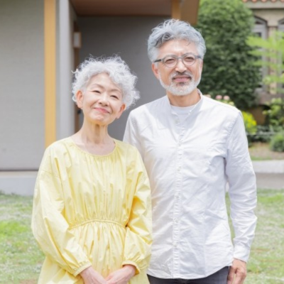 庭先で笑顔を見せるシニア夫婦の上半身