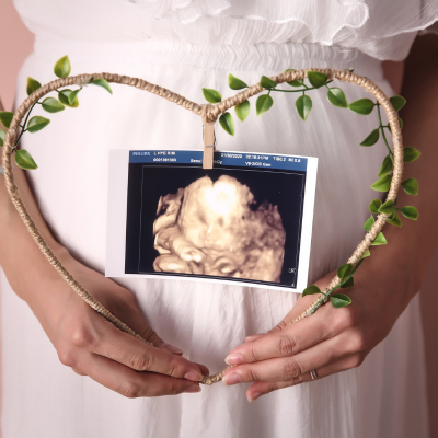 妊婦さんの手がハート型のリースを持ち、その中に胎児のエコー写真が見える様子
