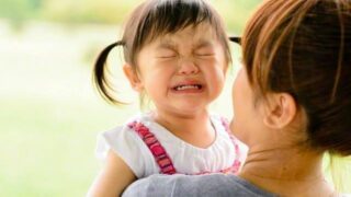 ママに抱っこされながら泣いてイヤイヤをする2歳の女の子